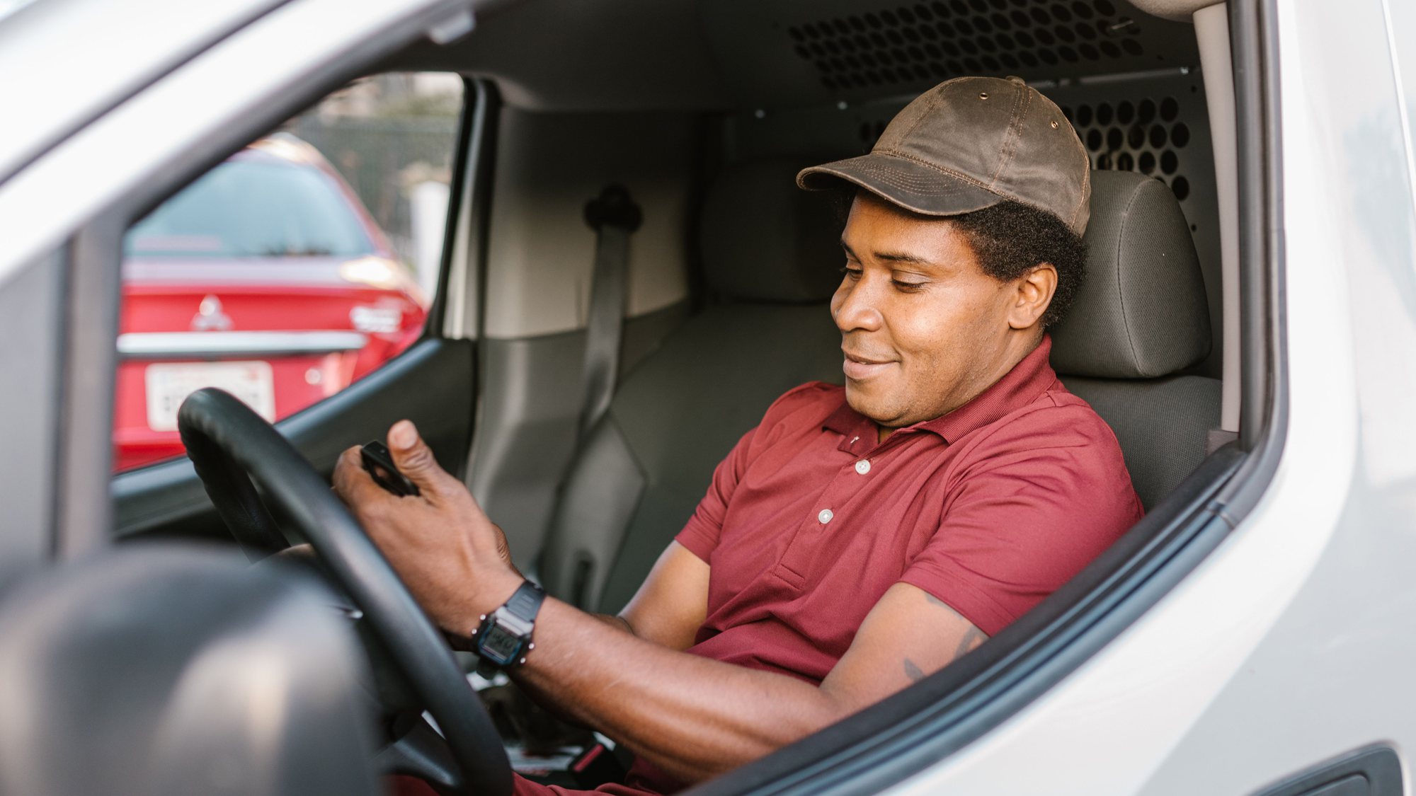 A contractor in the cab of a work van, checking his phone